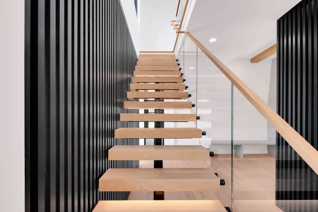 Minimalist Louisville floating staircase design with wood steps, glass railing, and black slat backdrop.