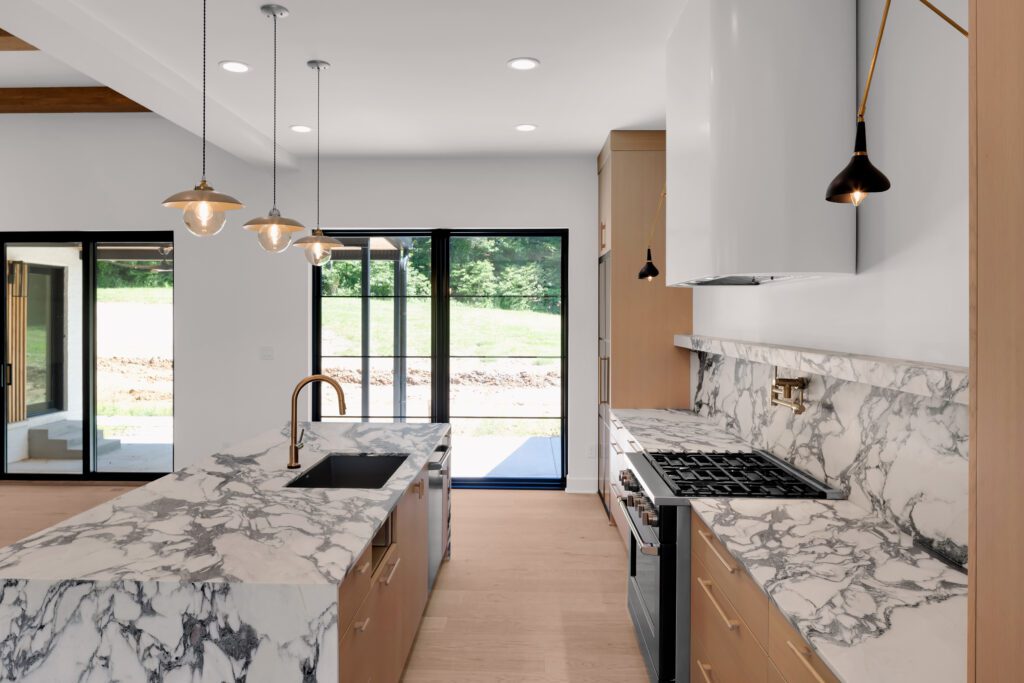 Contemporary Louisville kitchen with marble island, pendant lights, and greenery outside.