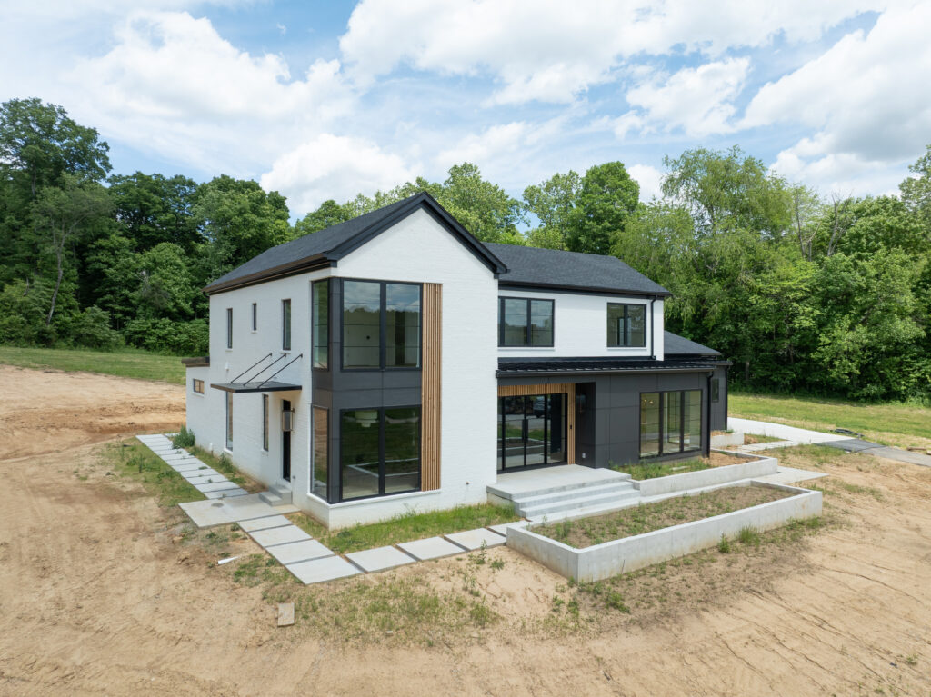 Contemporary Louisville home with sleek black accents, white brick facade, and lush green surroundings.