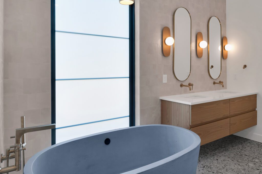 Louisville luxury bathroom featuring gray tub, wood vanity, oval mirrors, and wall sconces.