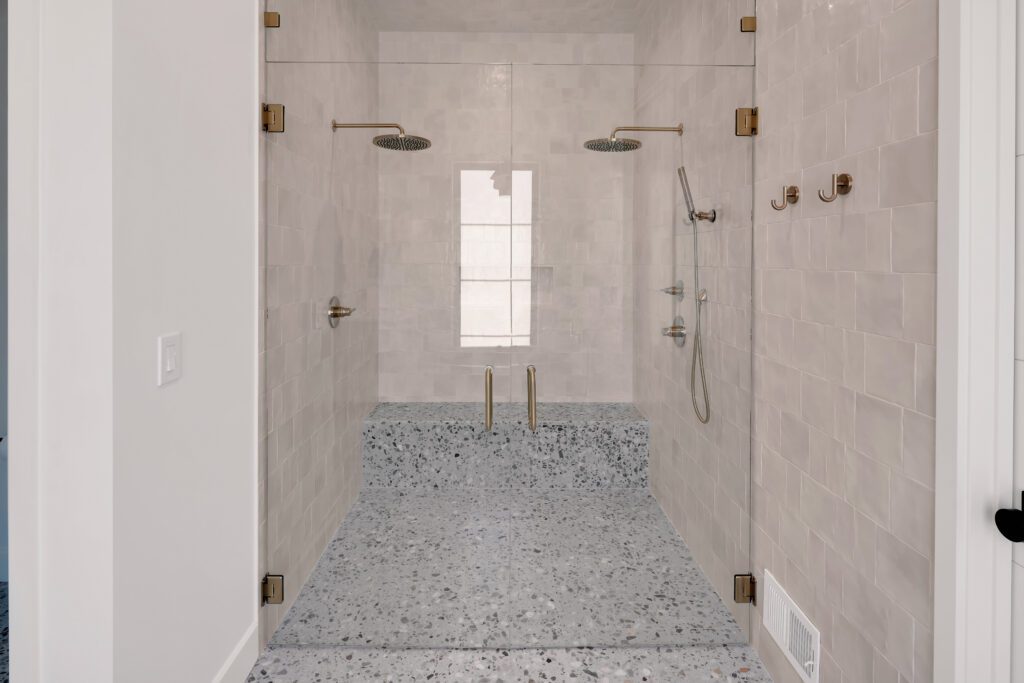 Minimalist Louisville custom home shower with terrazzo floor, glass doors, and chrome fittings.