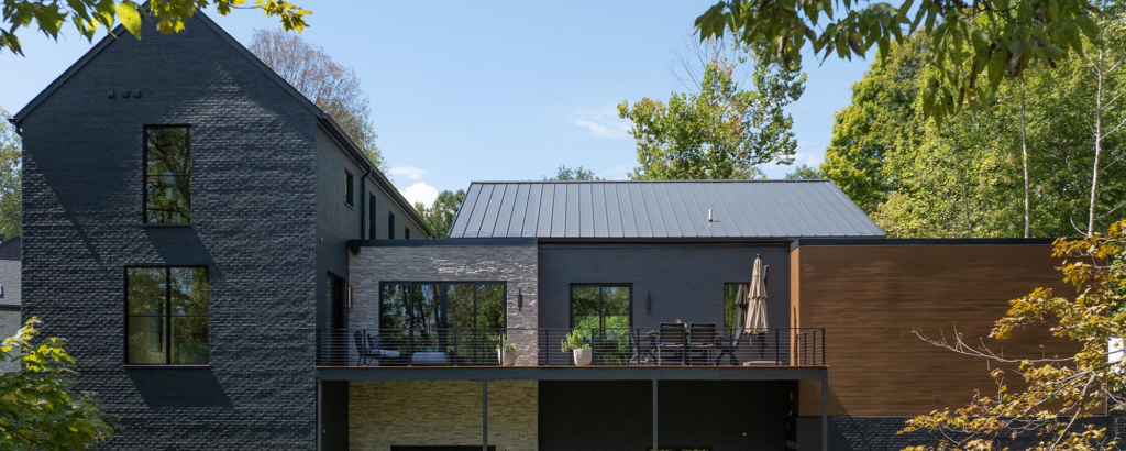 A modern Homearama house with dark brick, NewTechWood siding, and a balcony, showing a new custom home designed for a tranquil setting.