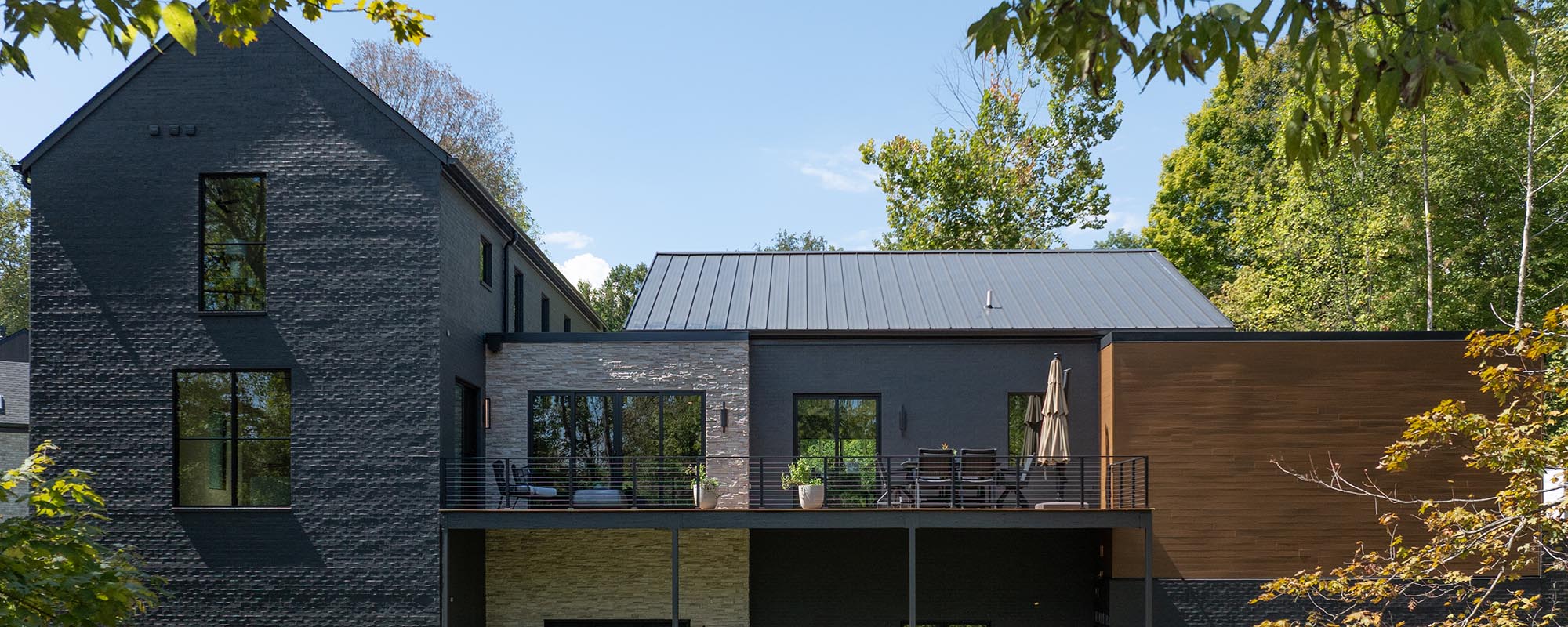 A modern Homearama house with dark brick, NewTechWood siding, and a balcony, showing a new custom home designed for a tranquil setting.