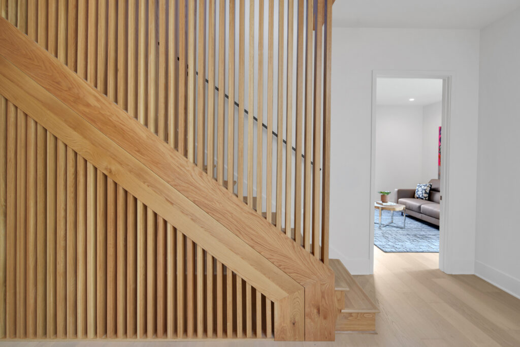 Louisville modern interior with wood-slatted staircase and a sitting room with gray sofa and blue rug by top custom home builders.