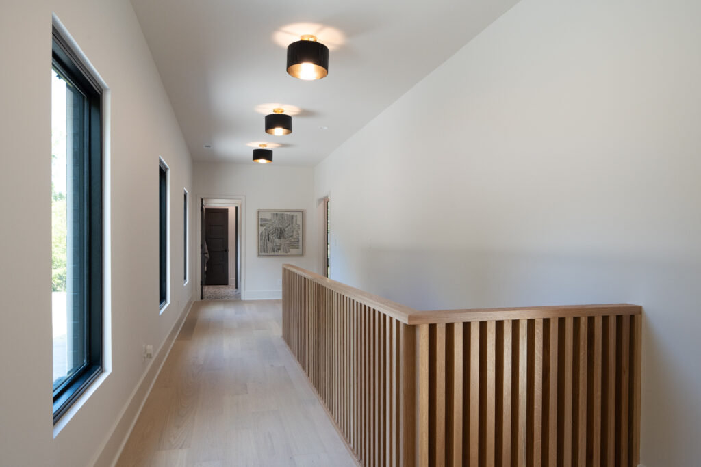 Louisville modern hallway with light wood flooring, sleek railing, and minimalist design by top custom home builders Eldridge Company.