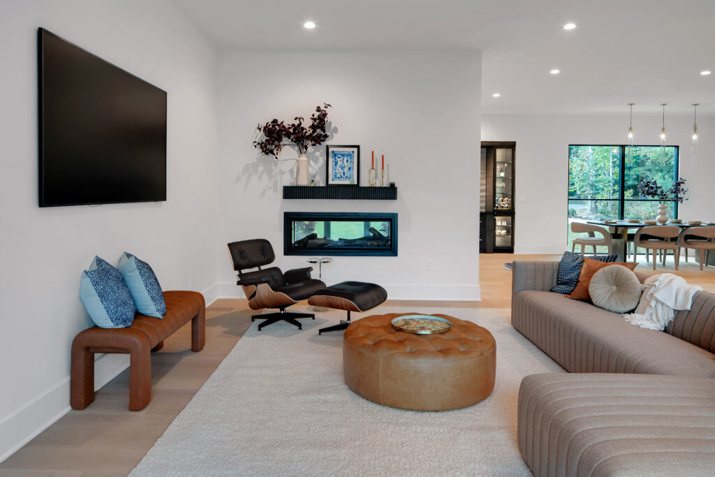 Contemporary Louisville living space at Homearama 2025 with cozy lounge, sectional sofa, wall-mounted TV, and serene garden views by custom builders.