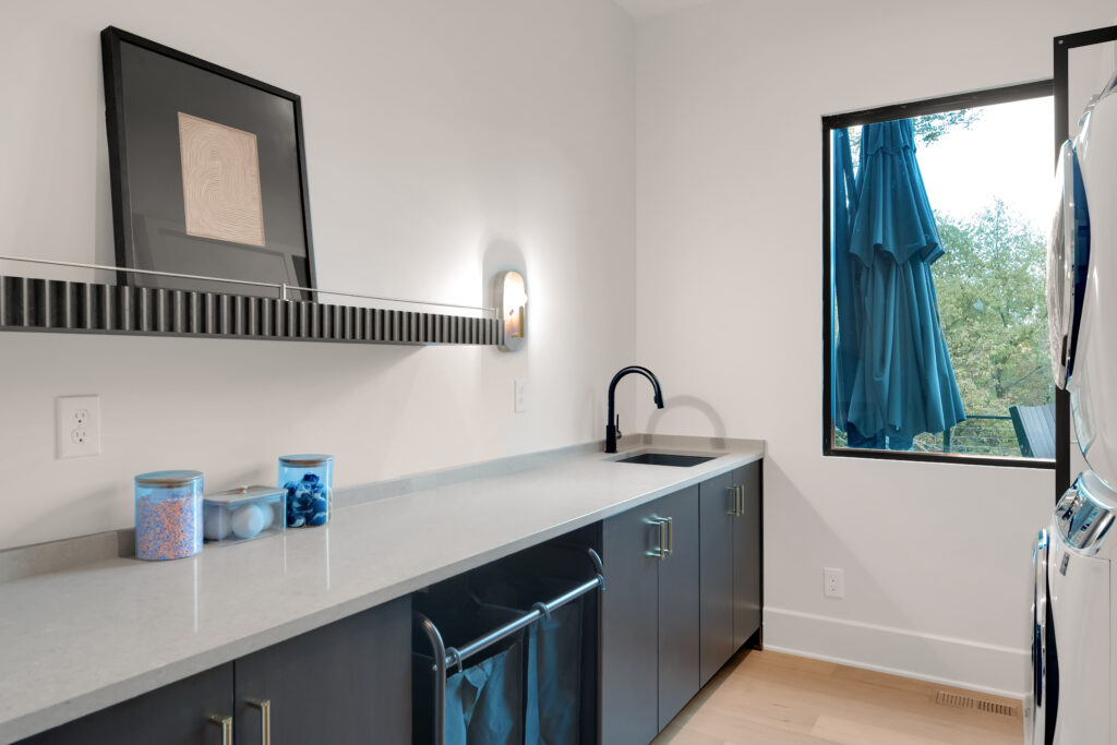 Modern Louisville laundry room with blue cabinets, stacked appliances, and black faucet by top custom home builders.