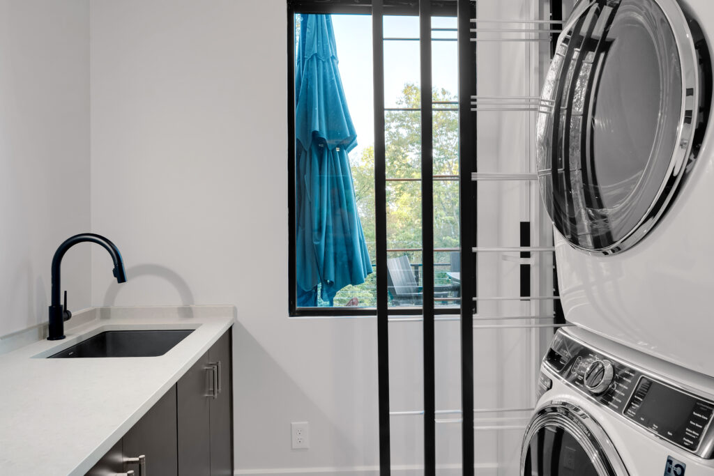 Modern Louisville laundry room with stacked washer and dryer, sleek countertop, and black faucet by top custom home builders.