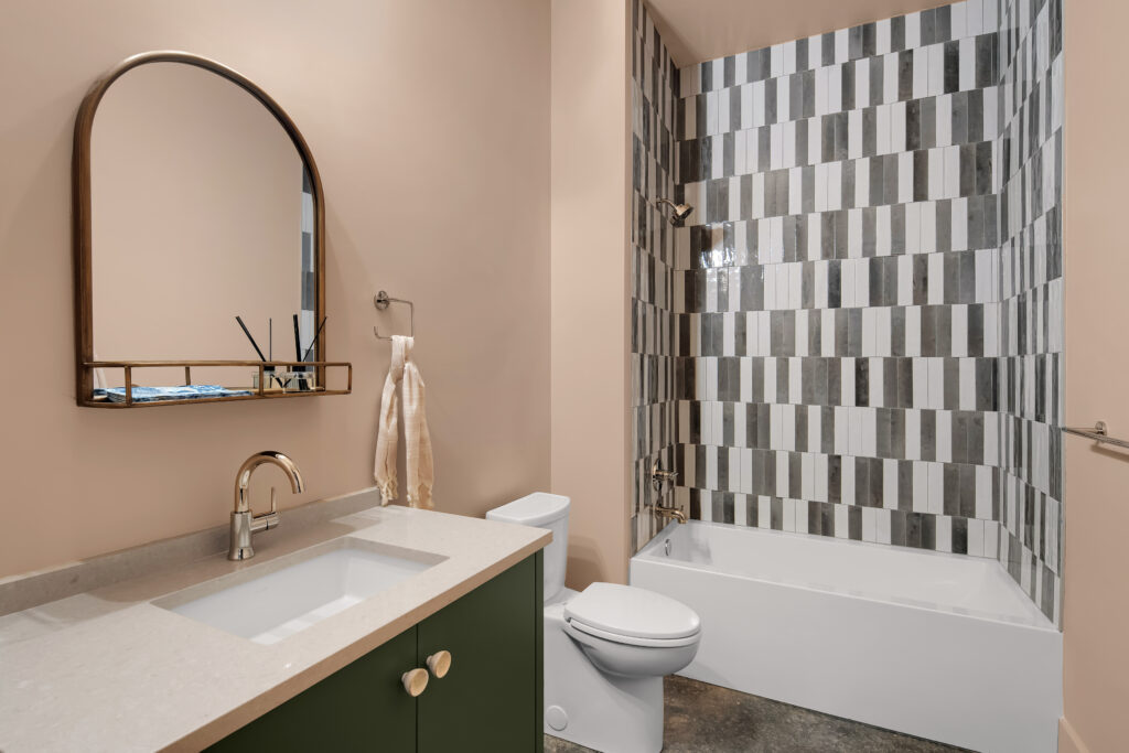 Louisville modern bathroom with green vanity, arched mirror, and striped tub tiles by top custom home builders.