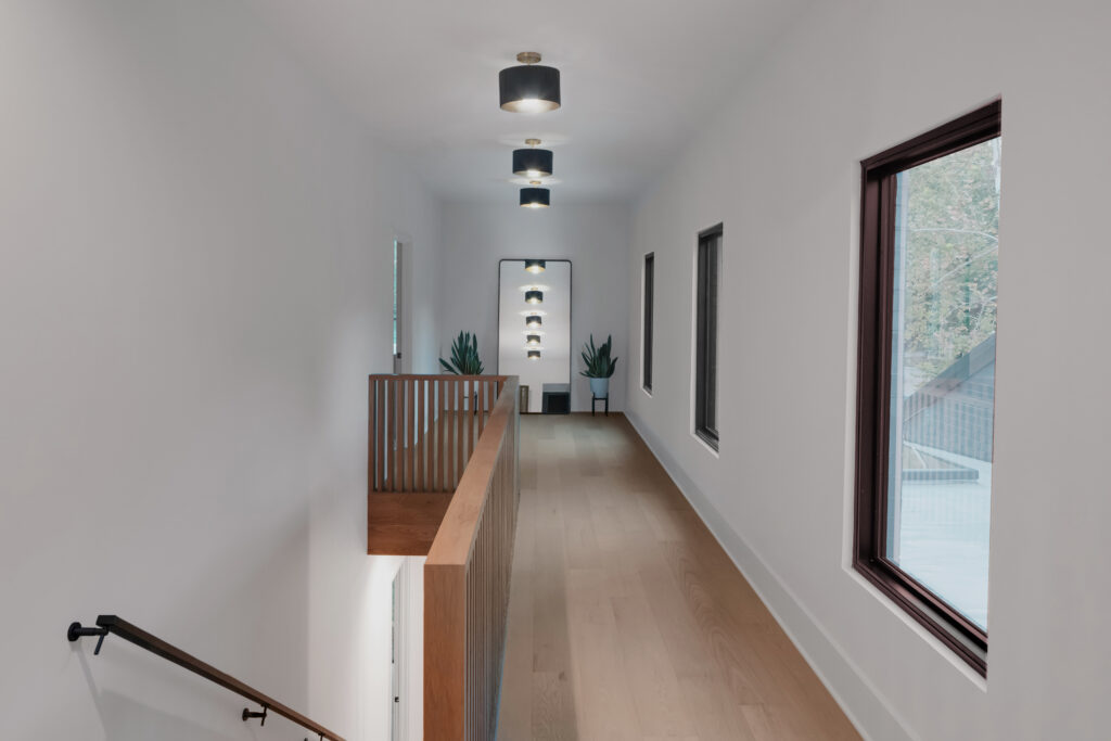 Louisville modern hallway with light wood floors, black ceiling lights, and airy design by top custom home builders.